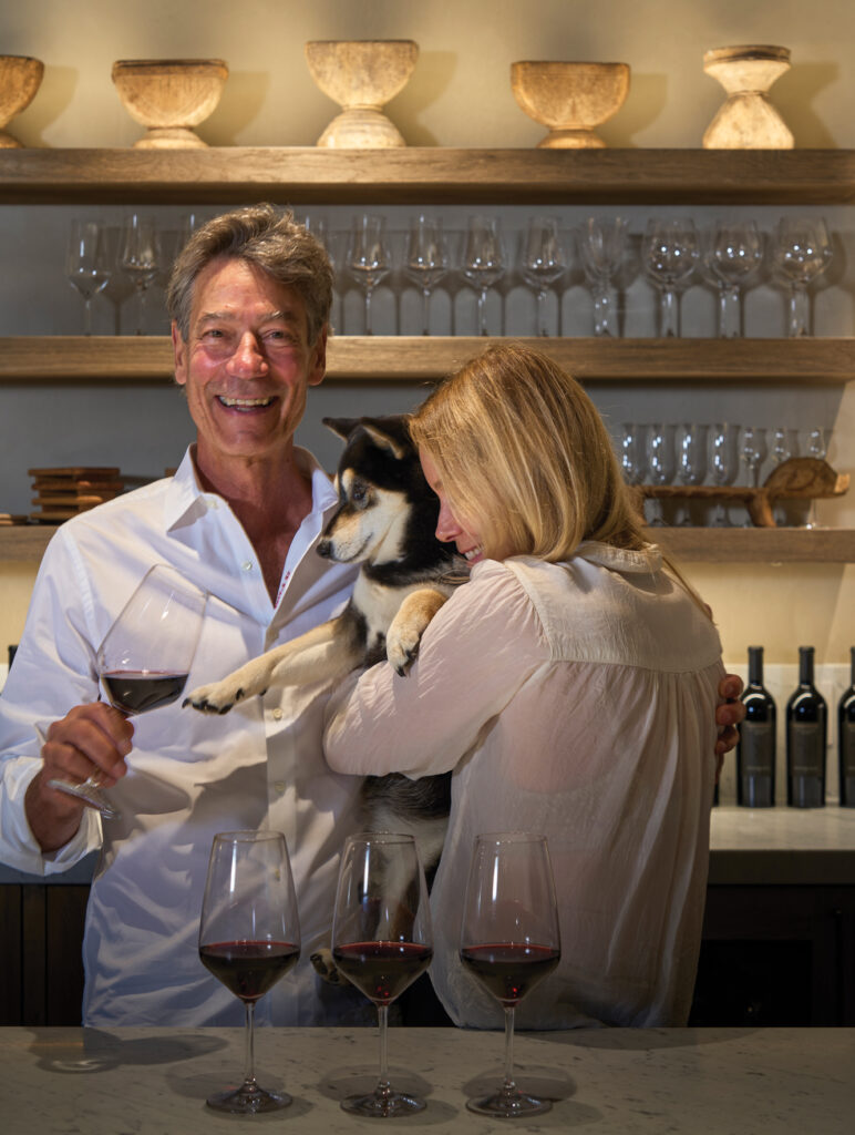 Couple smiling with their dog and several glasses of red wine