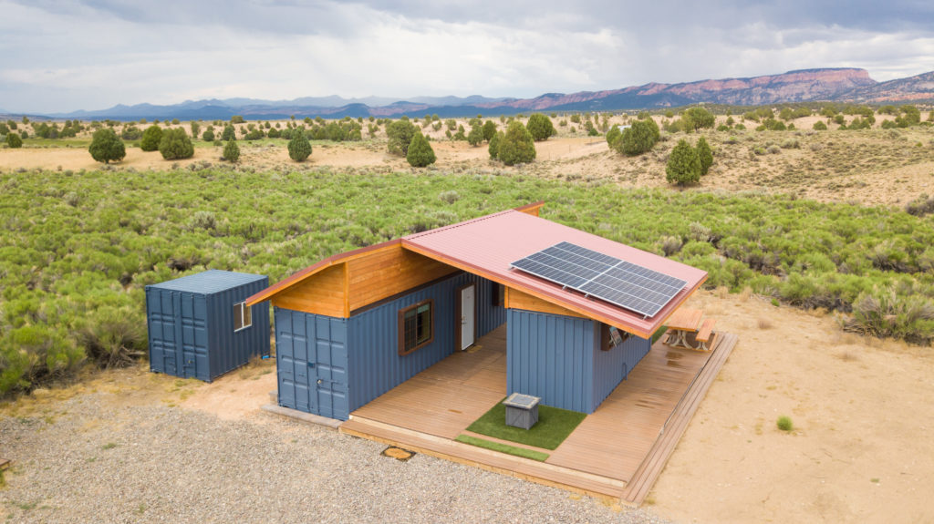 shipping containers repurposed into living quarters sit in a meadow in a large field in Utah.