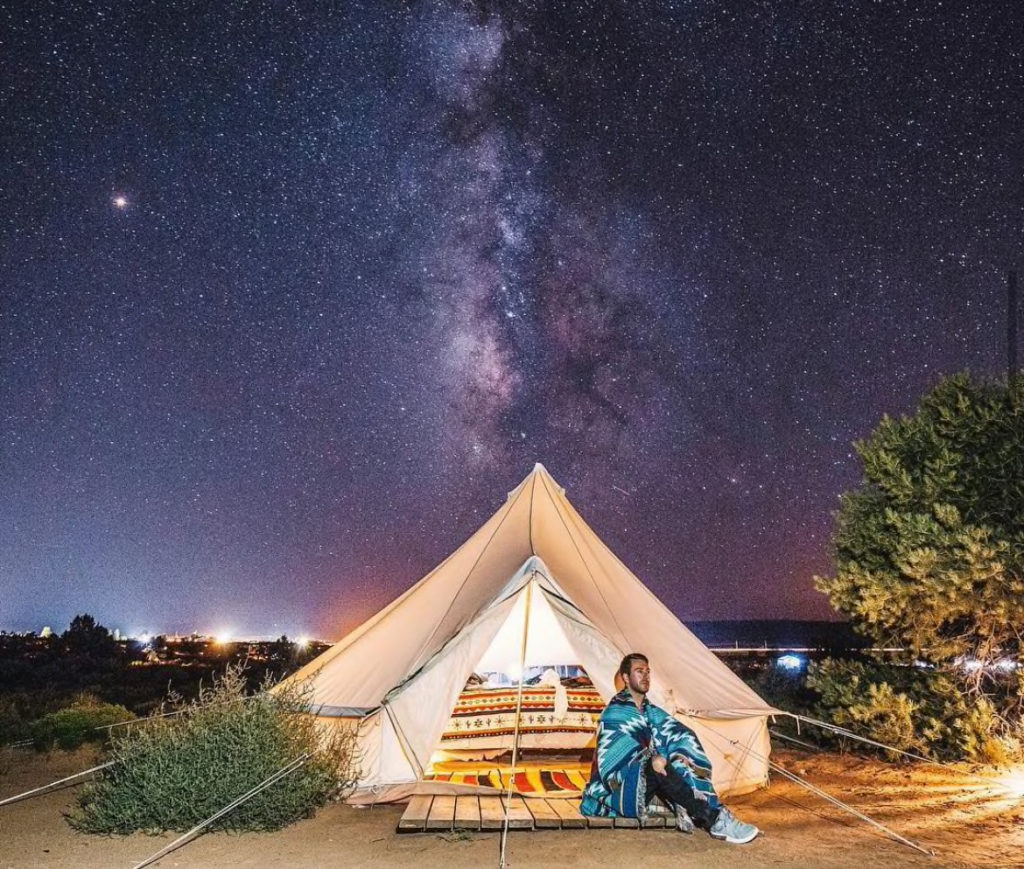 milky way visible over canvas tent with man sitting in foreground