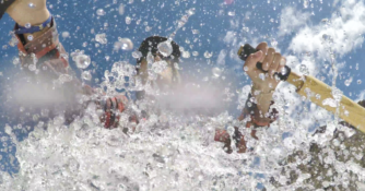 close up of person rowing a raft with splashing water suspended in air around them