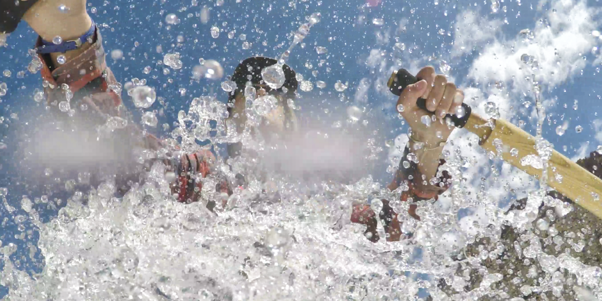close up of person rowing a raft with splashing water suspended in air around them