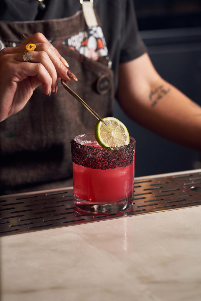 Bartender's hand using chopsticks to place a slice of lime into a cocktail.