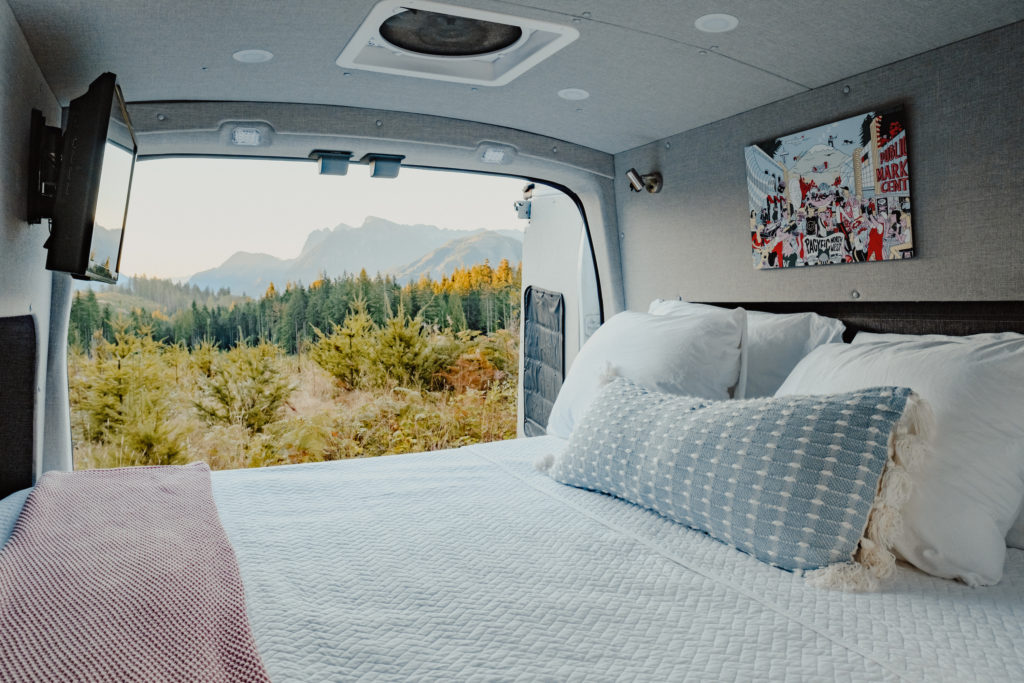 Cabana camper van interior with bed and view of trees and mountains