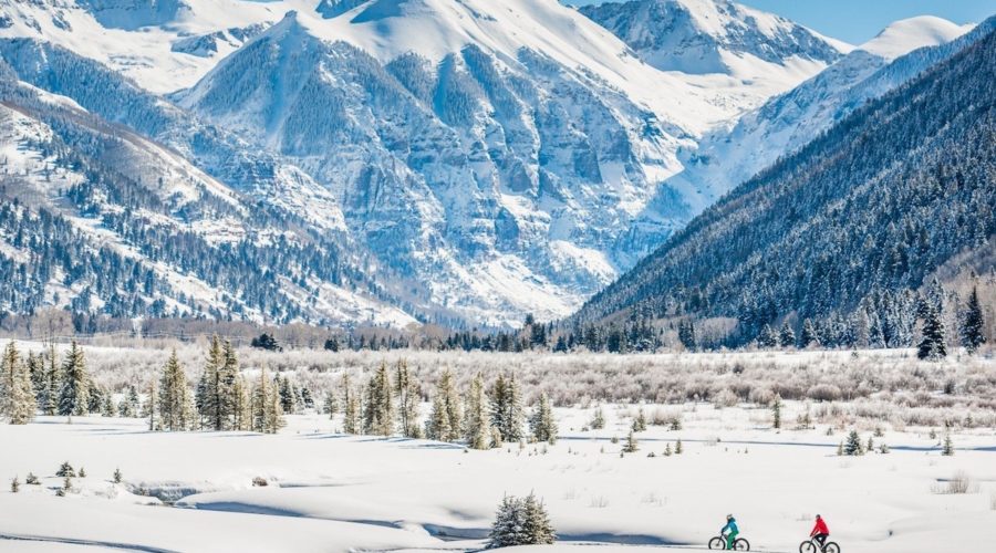 People fat tire biking through a valley with giant mountains in the background in snowy Telluride