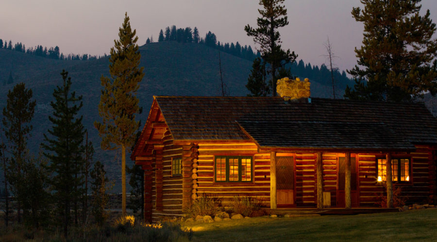 Nighttime view of cozy cabin illuminated under trees at Idaho Rocky Mountain Ranch