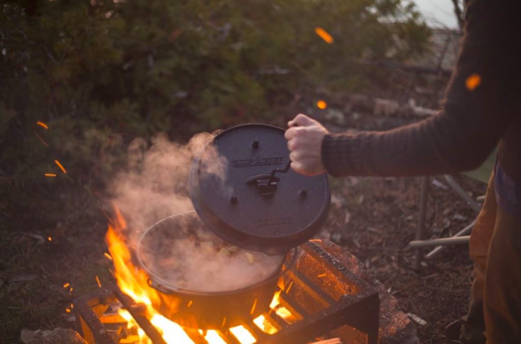 dutch oven being opened over roaring fire in the woods