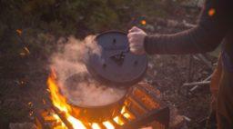 dutch oven being opened over roaring fire in the woods