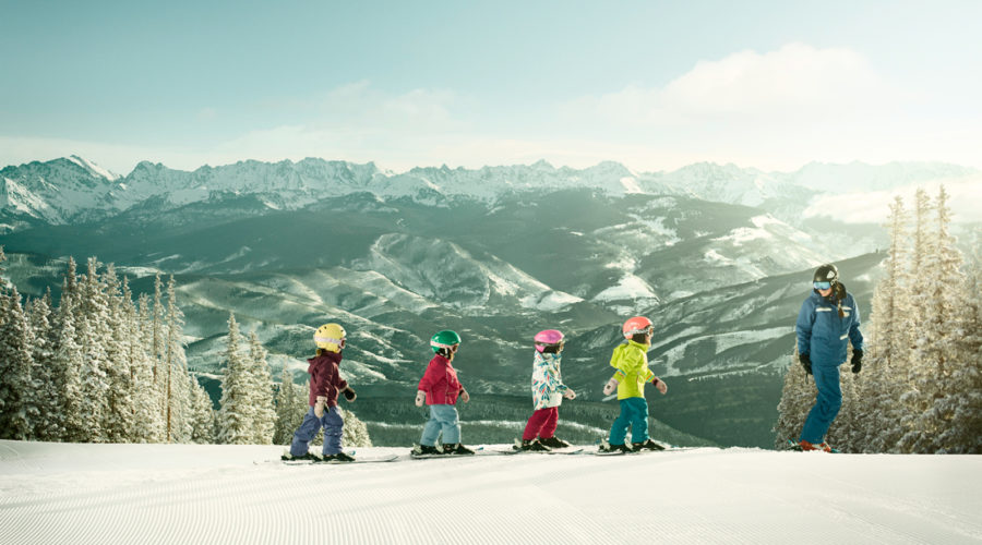 Four kids and an adult walking on top of mountain with skis at Beaver Creek