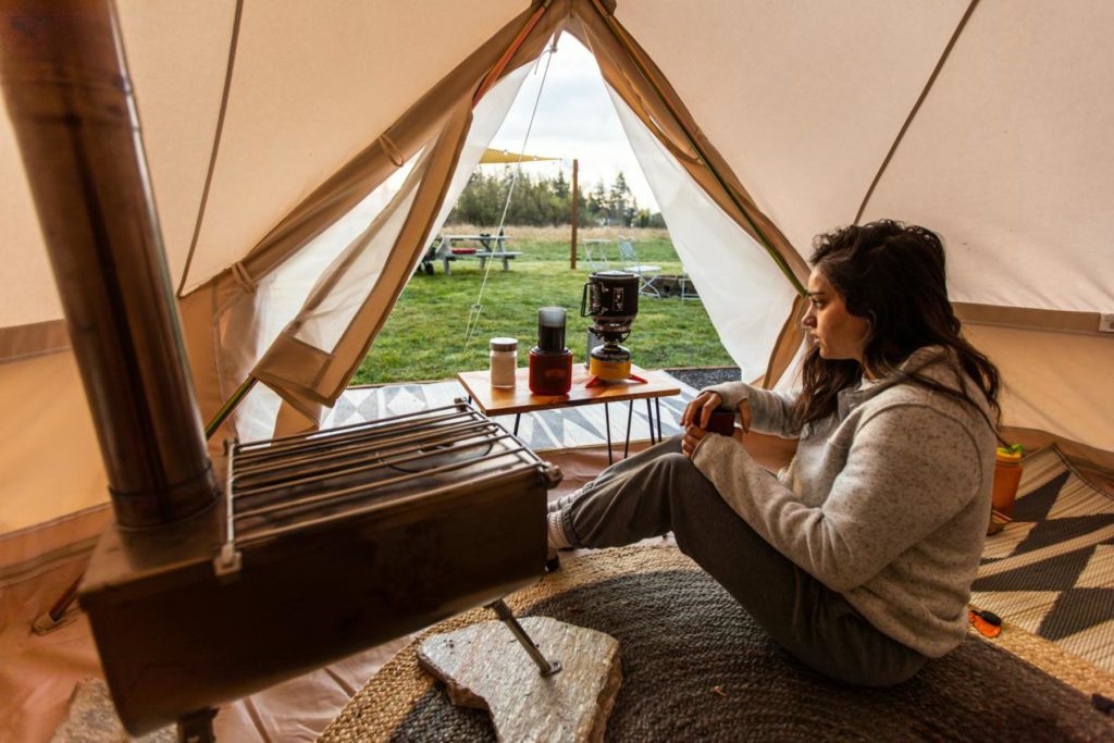 woman sits inside canvas tent next to stove