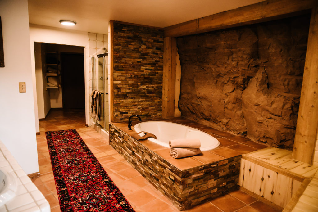 luxury soak tub with tiled stones at its base and cave wall on its side