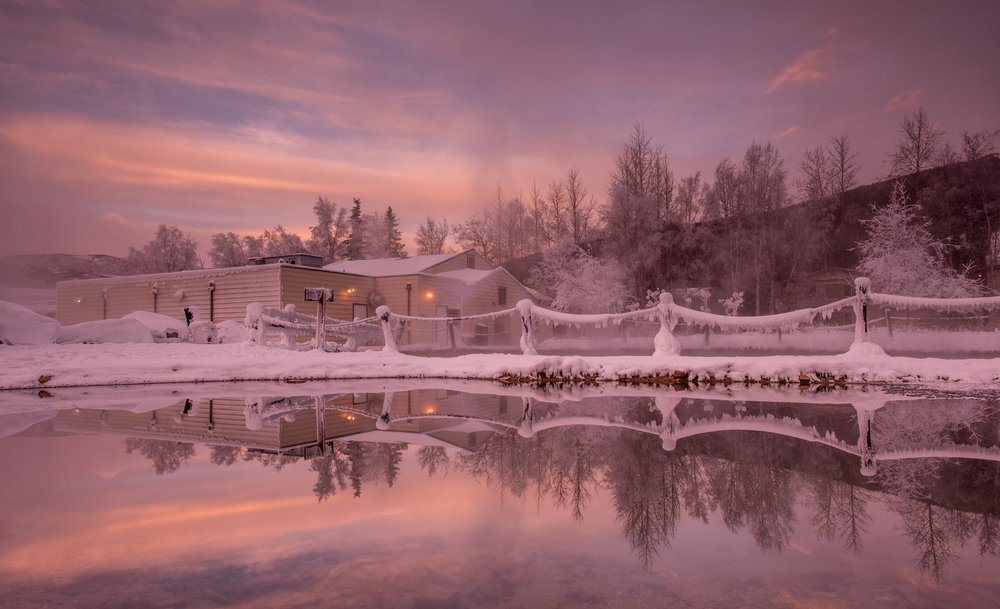 Chena Hot Springs covered in snow with pink sunset reflected off water