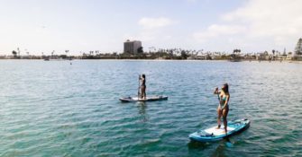 two people stand on two paddle boards that float on the water while they use oars to move