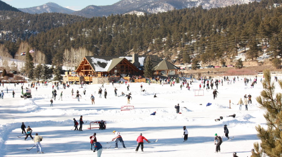 People ice skating and playing hockey on the Evergreen Lake ice skating rink with the mountains in the background