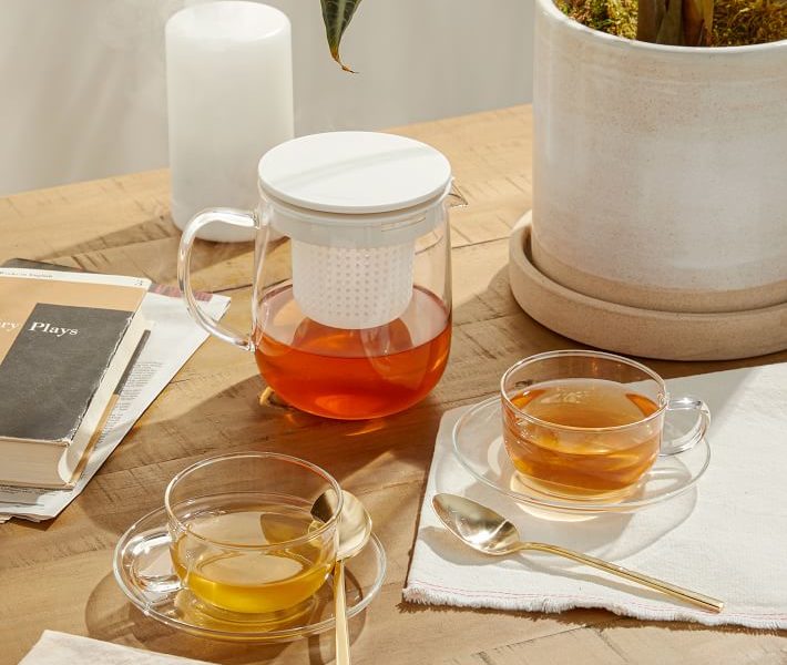 MUJI heat resistant tea set with glass teapot and teacups with saucers, displayed with red tea on wooden table.