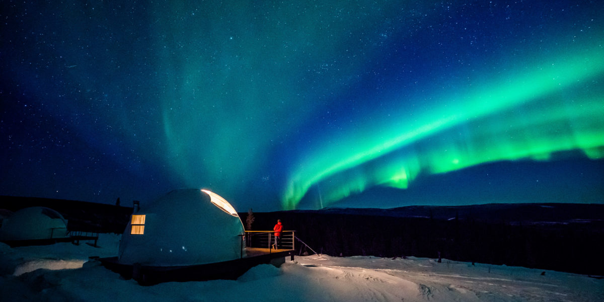Man standing on deck of a pod room at Borealis Basecamp watching northern lights