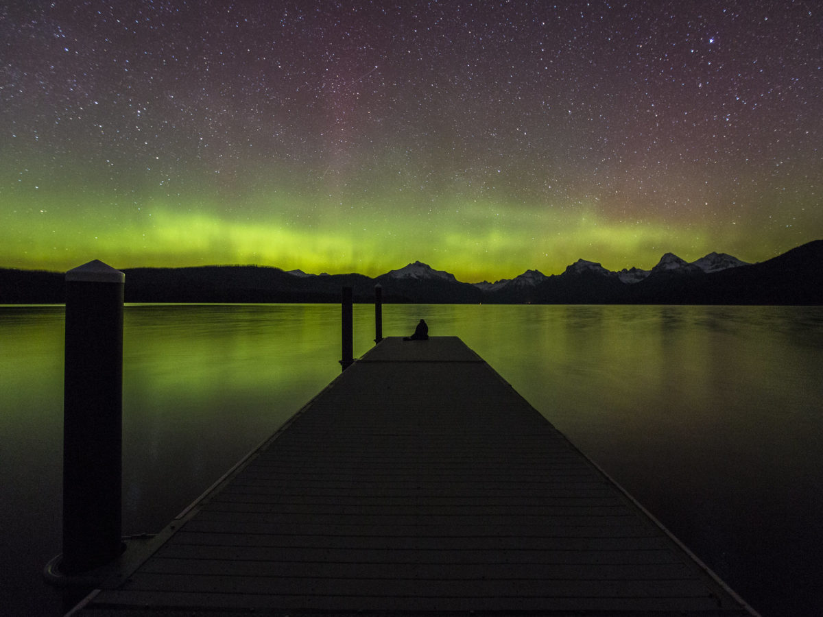 Person at end of dock watching northern lights in Glacier National Park