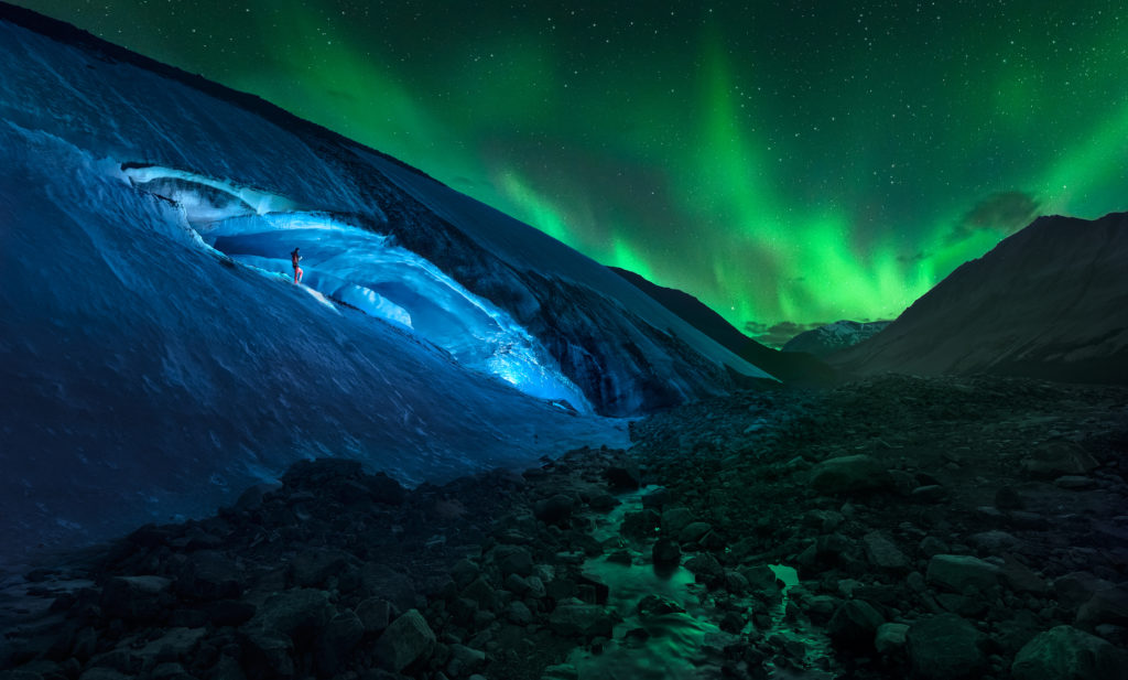 Person stands in Athabasca Cave entrance with northern lights overhead in Jasper