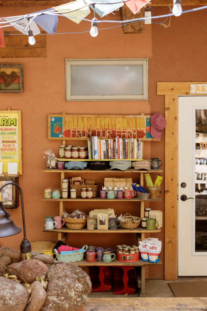 A shelving area with a sign saying, "Hell's Backbone Grill From Our Farm" and several jarred items, books, and more.