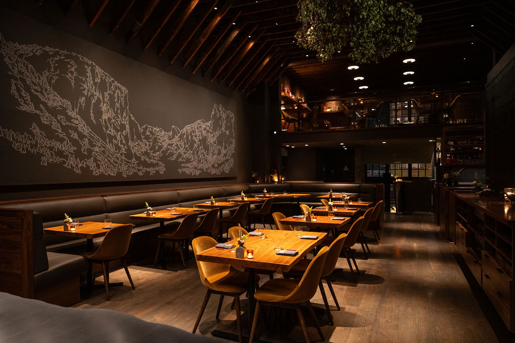 The interior of a restaurant with wooden tables and a mountain mural on the wall.