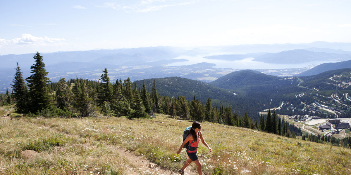 A woman hiking up Mt. Schweitzer while overlooking Sandpoint, Idaho, and Lake Pend Orielle.
