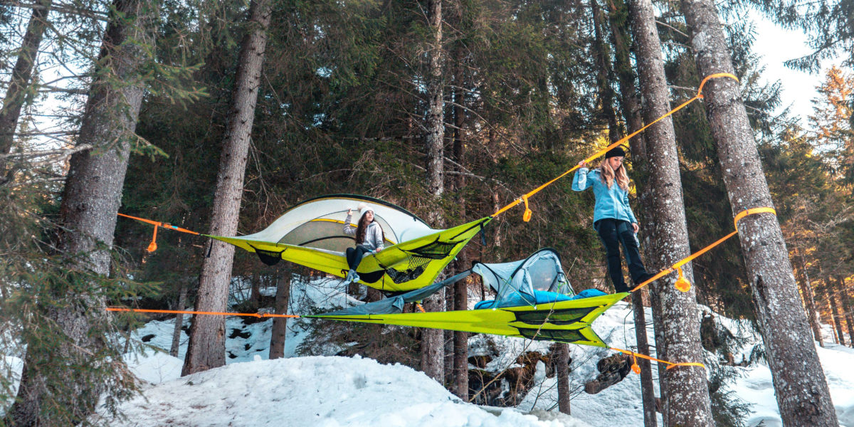 two tents suspended in air over forest floor covered in snow