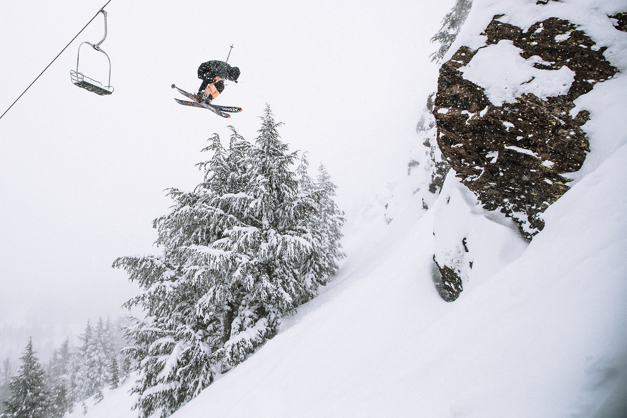 Skiers doing a flip while skiing at Mammoth slopes covered in snow with grey skies and snow falling