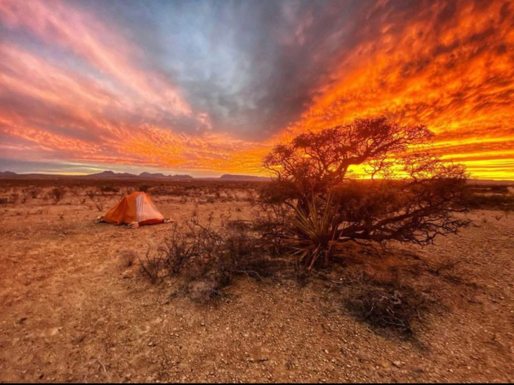 tent in the desert under a orange and red sky at sunset