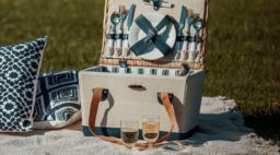 West Elm Park Picnic Basket 12 Piece Set in field with throw pillows and blanket.