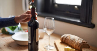 Person opening a bottle of wine on a wooden countertop.