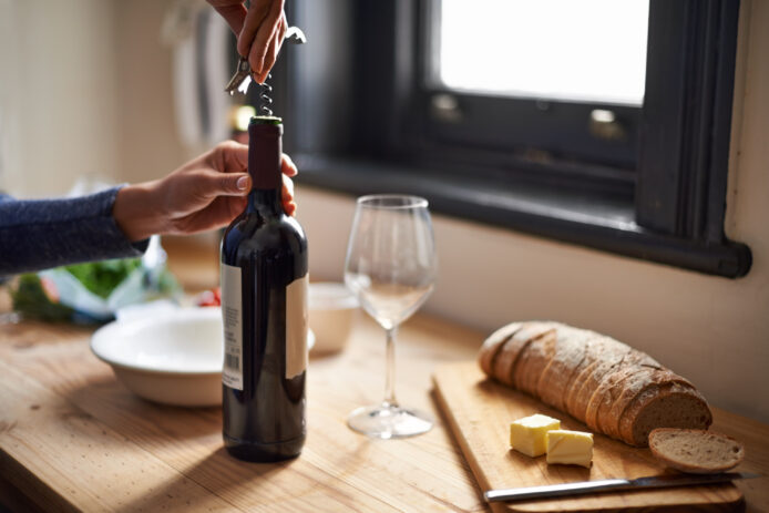 Person opening a bottle of wine on a wooden countertop.