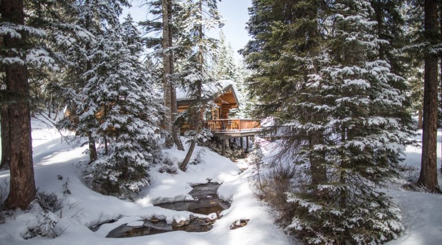 A cabin at Lone Mountain Ranch seen beyond the trees covered in snow in Montana